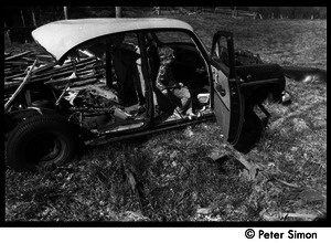 May Day at Packer Corners commune: child seated in a wrecked car