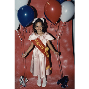 A girl wears a Caguas 1996 sash and holds balloons at the Festival Puertorriqueño