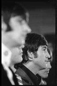 John Lennon at a Beatles press conference, with Ringo Starr in the foreground and George Harrison partly visible in the background