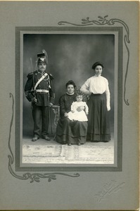 Polish American family portrait: studio portrait with mother and infant seated, man in military uniform with sword on shoulder