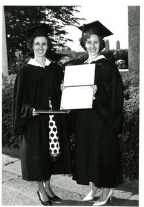 Twin sisters holding diplomas in their cap and gowns at the 1962 Suffolk University commencement