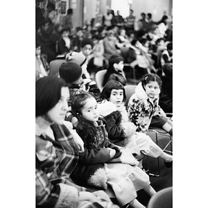 Audience watching the Three Kings' Day pageant at La Alianza Hispana, with a close-up view of a woman and three young girls seated together in a row