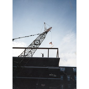 Construction worker on top of a platform guides a crane which lowers a steel beam bearing an American flag down on to the Taino Tower construction site.