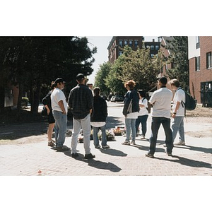 People gather for instructions prior to planting the flats of flowers that rest on the ground.