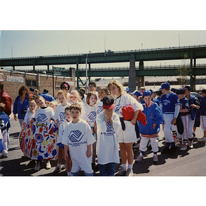 A group of children, wearing Boys and Girls Clubs of Boston t-shirts, pose with a banner displaying the text "Friendship," followed by another group wearing sports uniforms at the Boys and Girls Clubs of Boston 100th Anniversary Celebration Parade