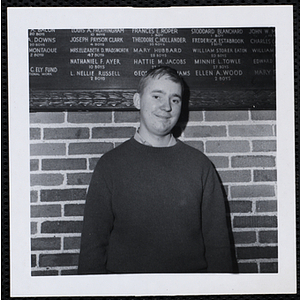 A male staff member posing in front of a brick wall with a commemorative plaque on it