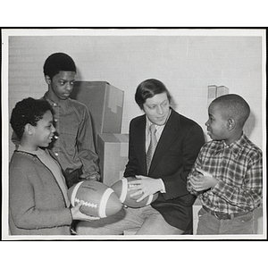 Former New England Patriot holding a football and talking to three Boys' Club members at a fund-raising event for the Boys' Clubs of Boston