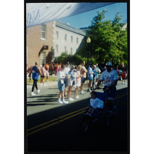 A man pushes a child in a stroller as he runs the Battle of Bunker Hill Road Race