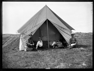 Three men seated around a tent on the dunes