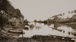 View of a river, two rowboats in the foreground and houses on both sides