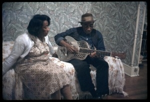 Mississippi John Hurt, seated on a hotel bed, playing guitar (at Newport?)