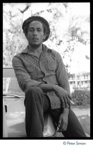 Bob Marley: half-length portrait at his house in Kingston, seated on the hood of his BMW, smoking a spliff