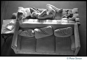 Overhead view of woman seated next to a sleeping Ram Dass on a couch, a Siamese cat by his side