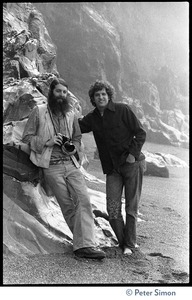 Rameshwar Das with camera, standing with Peter Simon by a granite outcropping on the beach