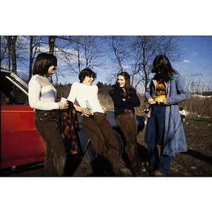 Four youths leaning against a car holding alcoholic beverages