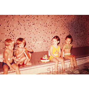Four children seated on the edge of a swimming pool