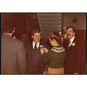 A woman pinning a carnation on a man's lapel while another man looks at the camera during a Boys' Club St. Patrick's Day event