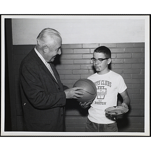 A man presents a basketball to a boy holding a plate at the Boys' Clubs of America Games Room Tournament