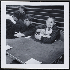 A boy sitting with his cat in his arms while another holds his dog during a Boys' Club Pet Show