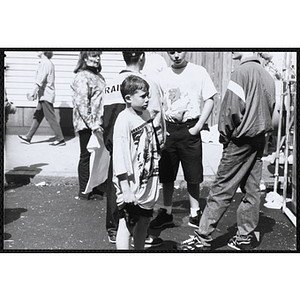 A boy looks to the front and grabs his t-shirt while a group of three boys stand beside him at the Boys and Girls Clubs of Boston 100th Anniversary Celebration Street Fair