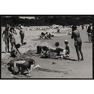 Children dig holes in the sand on a beach as other children and a woman look on