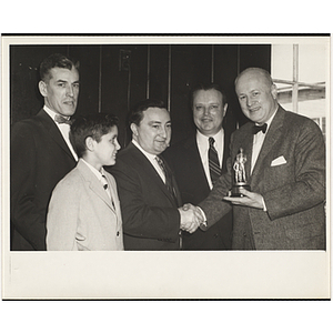 Arthur T. Burger, Executive Director of Boys' Clubs of Boston, holds a trophy and shakes hands with State Senator John E. Powers while others stand by during a Boys' Clubs of Boston awards event
