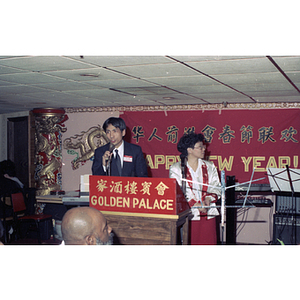 Suzanne Lee stands next to a man who speaks at a podium during a Chinese Progressive Association celebration of the Chinese New Year