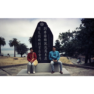 Two Association members sit at the base of a Chinese monument on Angel Island