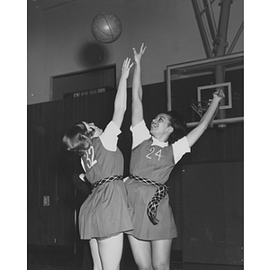 Two female students reach for a basketball in the air