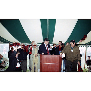 Neal Finnegan stands at the podium as students wave pompoms behind him at a Harvard football game