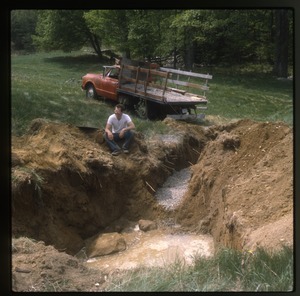 Dan Keller seated by excavated pit, pickup truck in background, Wendell Farm