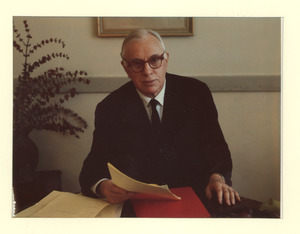 Louis M. Lyons sitting indoors, behind desk