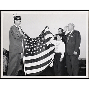 Arthur T. Burger, Boys' Clubs of Boston Executive Director, at far right, and a Boys' Club member salute a man wearing a veteran cap as he holds an American flag with another man