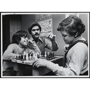 A man instructs two boys playing chess
