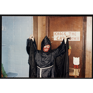 A child in a Halloween costume poses in front a "Knock the Cat Down" game