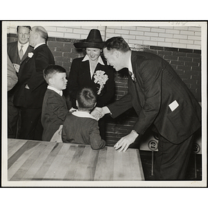 A man shakes hands with a boy as a woman and another boy look on at the dedication and cornerstone laying ceremony for the Charles Hayden Memorial Clubhouse in South Boston