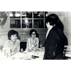 Guest talks to two men selling books, periodicals, and publications in the lobby of the Josiah Quincy School at a program about the normalization of U.S. and China relations