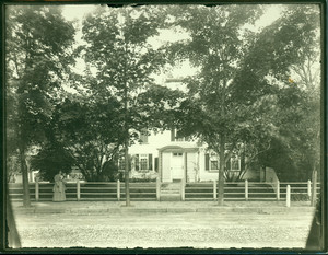 Woman standing next to the front fence of the Cooper-Frost-Austin House, Cambridge, Mass., undated
