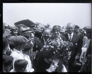 Amelia Earhart reception: Earhart with bouquet of flowers, being whisked through the crowd at the East Boston airport