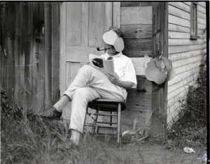 George Allan England reading outside a cabin while wearing an oversized visor