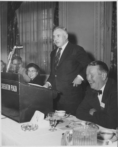 Louis M. Lyons standing indoors, speaking at podium