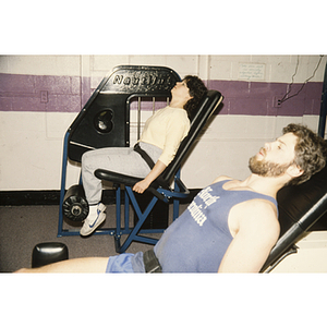 Man and woman work out on weightlifting machines in a gym