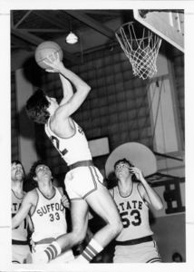Suffolk University men's basketball player Bob Ferrara (#12) goes up for two points during a game as Suffolk player Chris Tsiotos (#33) looks on, 1975