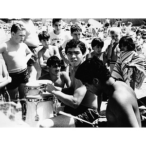 Group of Latino children listen to two youths playing the drums at the beach, at an outing sponsored by La Alianza Hispana.