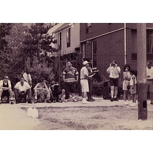 People standing and sitting around the edges of a grassy area behind Villa Victoria townhouses.