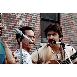 Men singing and making music against a backdrop of a brick wall.
