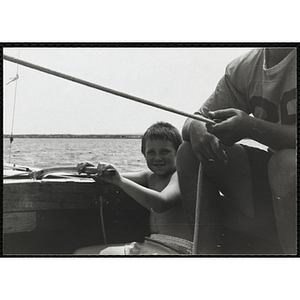 A boy sits on the deck of a sailboat in Boston Harbor