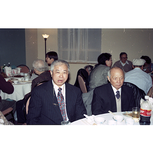 Two men sit at a restaurant table during a Chinese Progressive Association celebration of the Chinese New Year