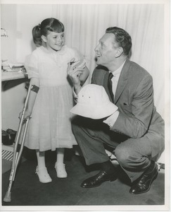 Unidentified man signing hat for young girl with forearm crutch