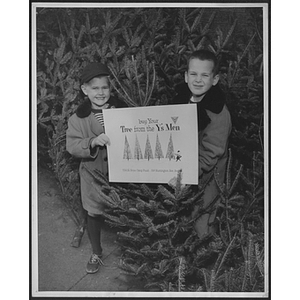 Two children at Christmas tree sale holding up sign